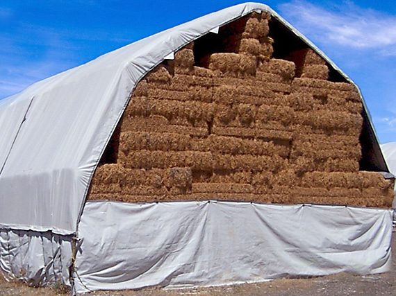 Hay tarp with cam-lock strapping covering a stack of bales